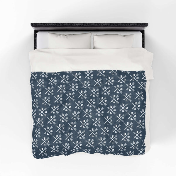PNW Arrow Crossroads Lightweight Cozy Blanket on a bed, featuring a stylish crossed arrows design.