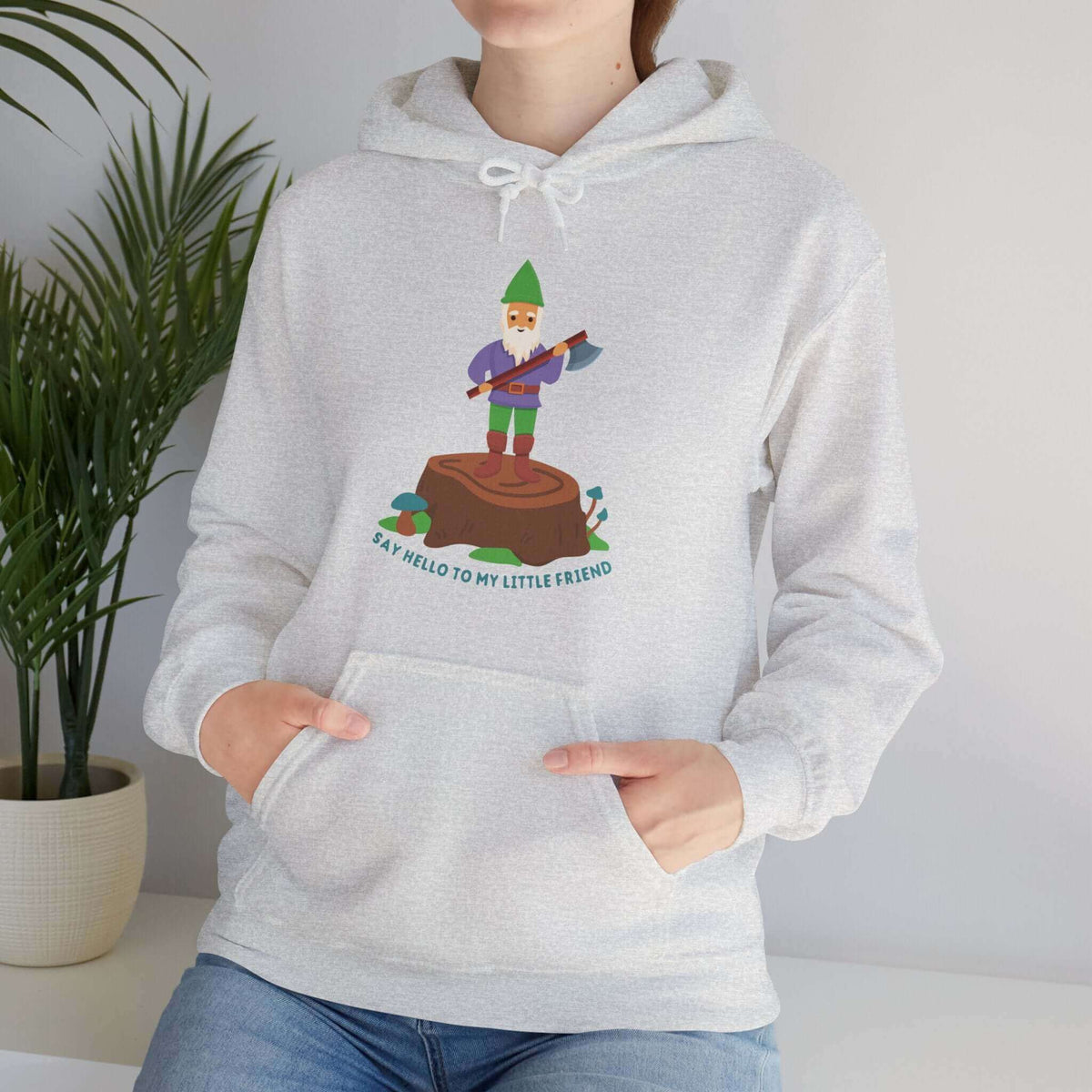 Woman wearing a hoodie with a gnome holding an axe, standing on a stump, and the text 'Say Hello to My Little Friend.' Funny style sweatshirt.