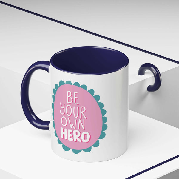 Be Your Own Hero Mug featuring a pink badge and teal scallops on a white ceramic design.