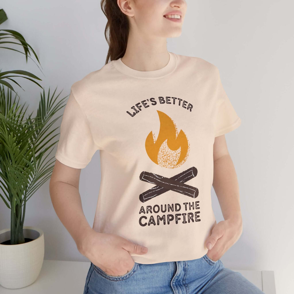 Woman wearing a Life's Better Around the Campfire T Shirt with a campfire design, ideal for outdoor lovers.