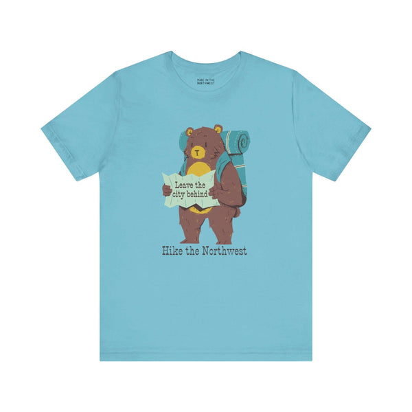 Light blue tee featuring a bear with backpack and map, captioned "Leave the city behind, Hike the Northwest" for outdoor adventure lovers.