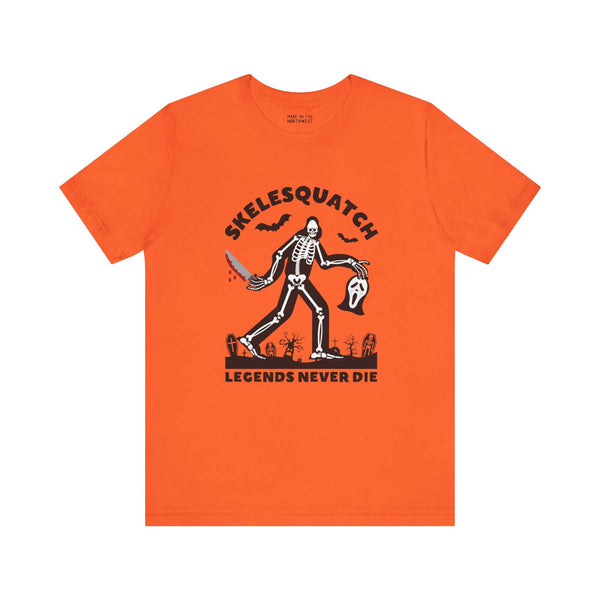 Skelesquatch Halloween tee featuring a skeleton sasquatch with a bloody knife and Scream mask in a graveyard on an orange shirt