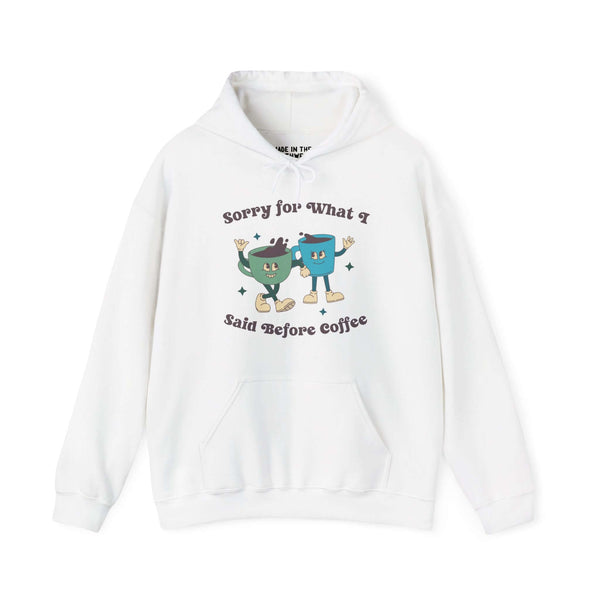 White hoodie with playful "Sorry for What I Said Before Coffee" design, featuring cartoon cups, ideal for coffee lovers.