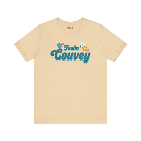 Beige retro tee featuring "Feelin' Couvey" text with aqua and pink flowers celebrating Vancouver, WA.
