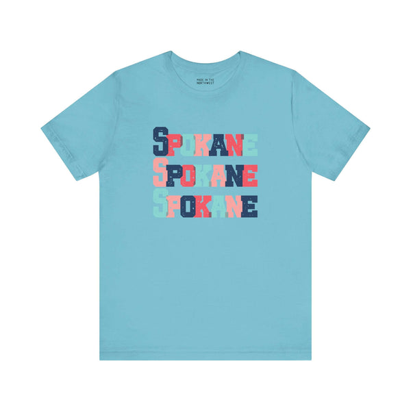 Blue Spokane t-shirt with bold, colorful block-letter design showcasing the city name stacked in vibrant hues.