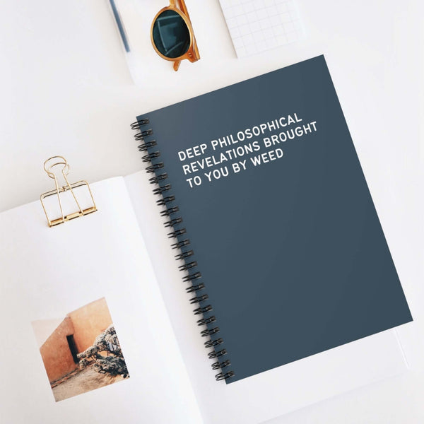 Dark blue spiral notebook titled 'Deep Philosophical Revelations Brought to You By Weed' on a minimalistic desk.
