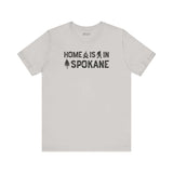 Home Is in Spokane Tee featuring campfire, Bigfoot, and tree illustrations celebrating Spokane's outdoor spirit.