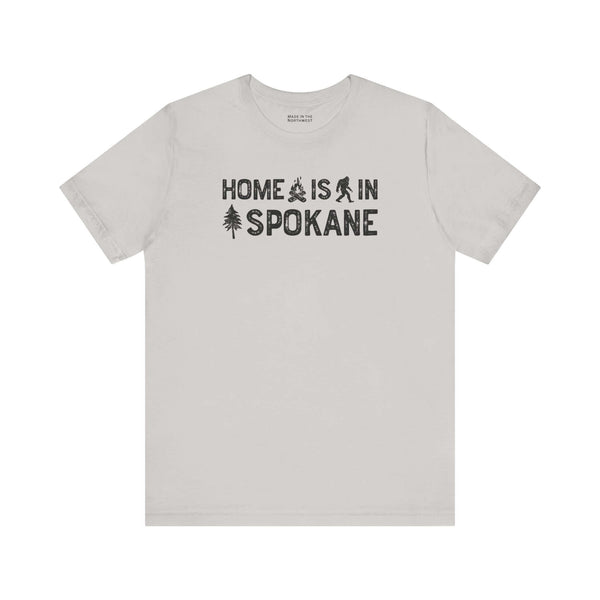 Home Is in Spokane Tee featuring campfire, Bigfoot, and tree illustrations celebrating Spokane's outdoor spirit.