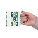 Hand holding a colorful Five-Oh-Three Pop ceramic mug showcasing bold green and blue designs, celebrating Portland's spirit.