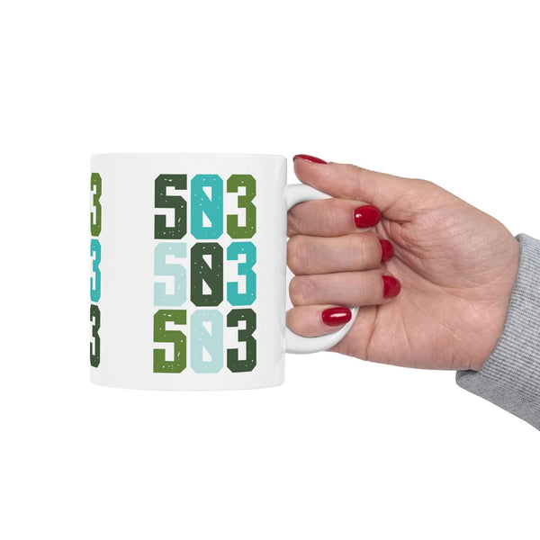 Hand holding a colorful Five-Oh-Three Pop ceramic mug showcasing bold green and blue designs, celebrating Portland's spirit.