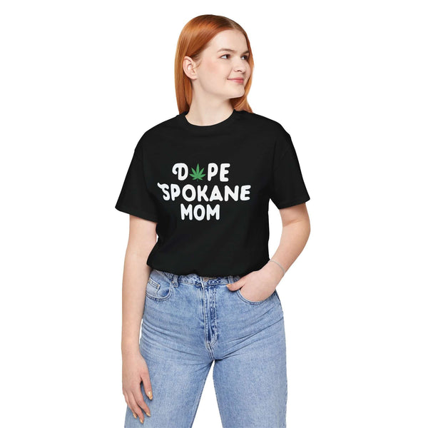 Woman wearing "Dope Spokane Mom" black tee with a marijuana leaf design, casual style in jeans.