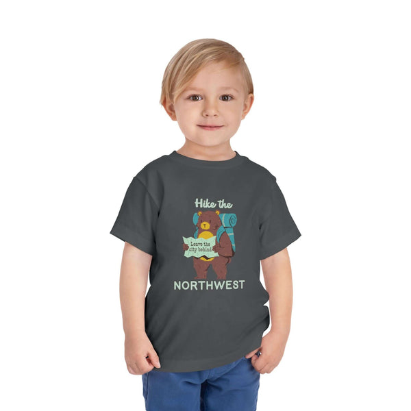 A toddler wearing a dark grey Hike the Northwest toddler tee featuring a bear with a map, perfect for little explorers.