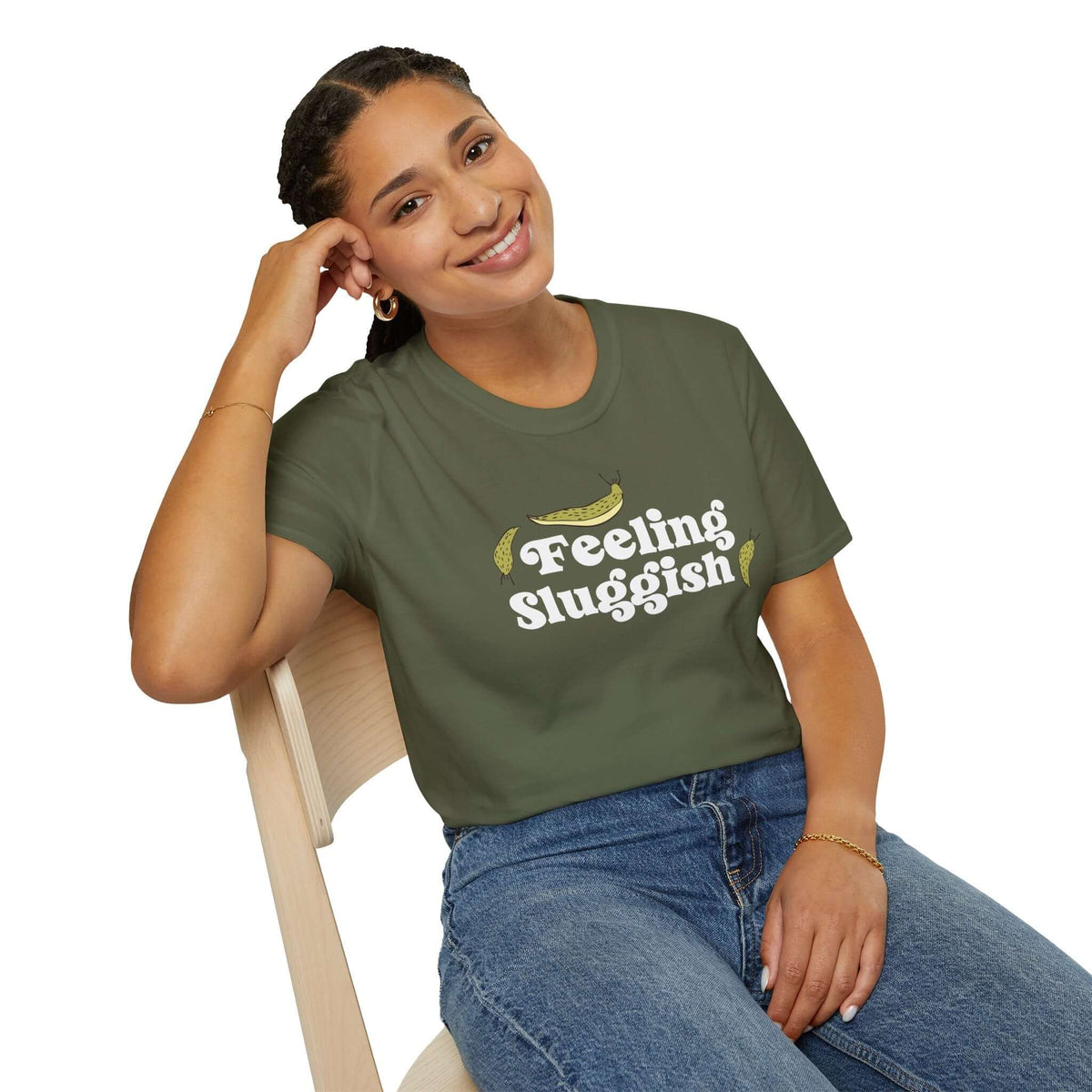 Smiling woman wearing a Feeling Sluggish T Shirt while seated on a chair, promoting cozy vibes.
