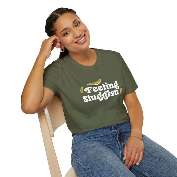 Smiling woman wearing a Feeling Sluggish T Shirt while seated on a chair, promoting cozy vibes.