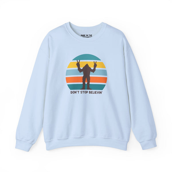 Light blue sweatshirt with 'Don't Stop Believin'' text and playful Bigfoot graphic on a striped background.