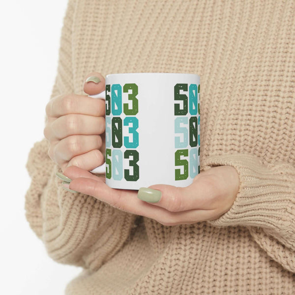 Colorful Five-Oh-Three Pop Ceramic Mug showcasing Portland's spirit, held by a person in a cozy sweater.