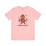 Pink tee shirt featuring a whimsical Sasquatch graphic and the phrase 