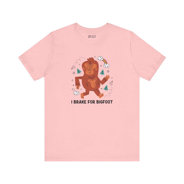 Pink tee shirt featuring a whimsical Sasquatch graphic and the phrase "I Brake for Bigfoot" for folklore enthusiasts.