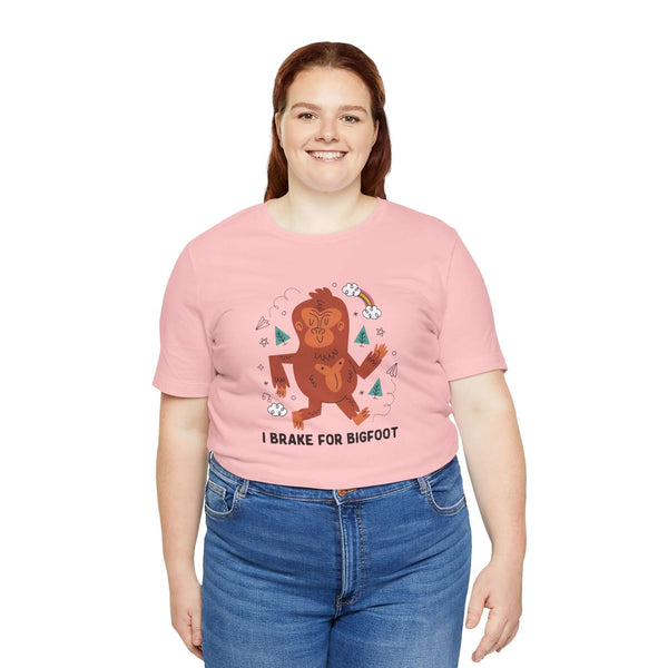 Model wearing a pink 'I Brake for Bigfoot' tee with whimsical Sasquatch graphic, celebrating local folklore.