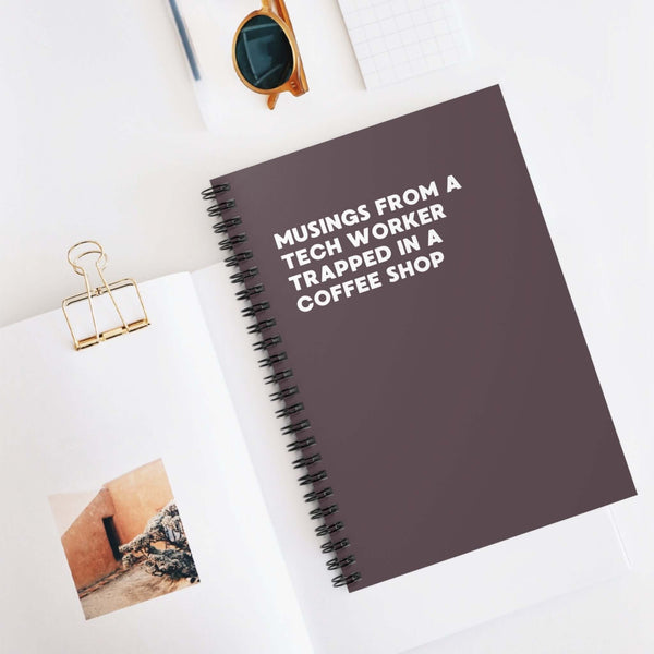 Spiral notebook titled 'Musings from a Tech Worker Trapped in a Coffee Shop' on a desk.