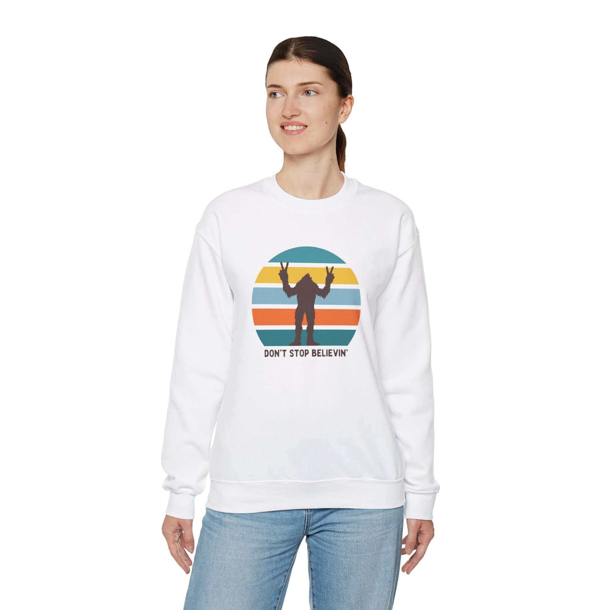 Woman wearing a "Don't Stop Believin'" Bigfoot sweatshirt with colorful stripes and sasquatch graphic.