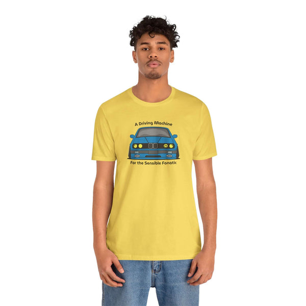 Model wearing a yellow tee featuring a BMW E30 325is and text: A Driving Machine for the Sensible Fanatic.