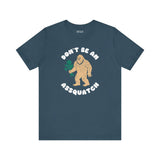 Don’t Be an Assquatch Tee featuring a friendly Bigfoot holding flowers on a navy shirt.
