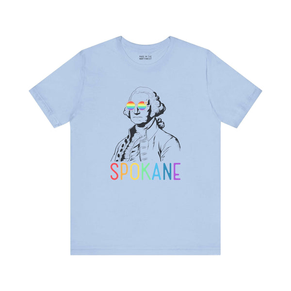 Light blue Spokane tee with rainbow "Spokane" text and line art of George Washington wearing rainbow glasses, celebrating Pride.