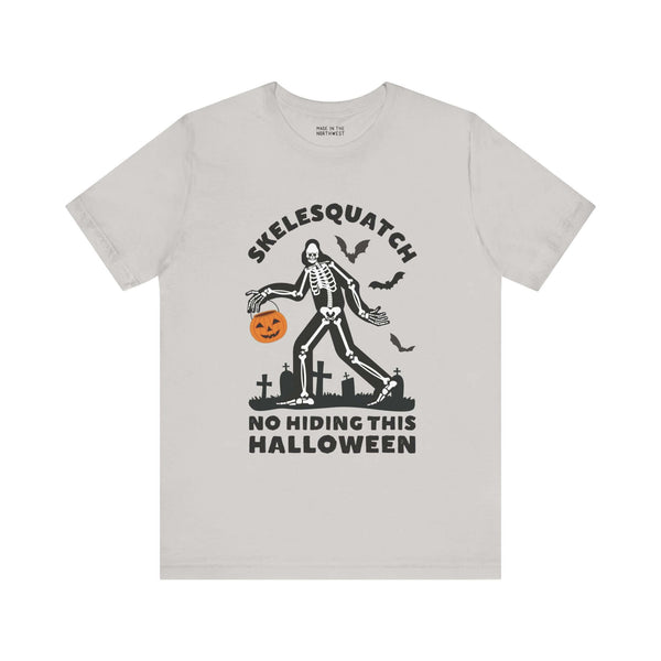 Halloween Skelesquatch tee featuring skeleton Sasquatch in graveyard with trick-or-treat bucket, perfect for spooky and cryptid fun.