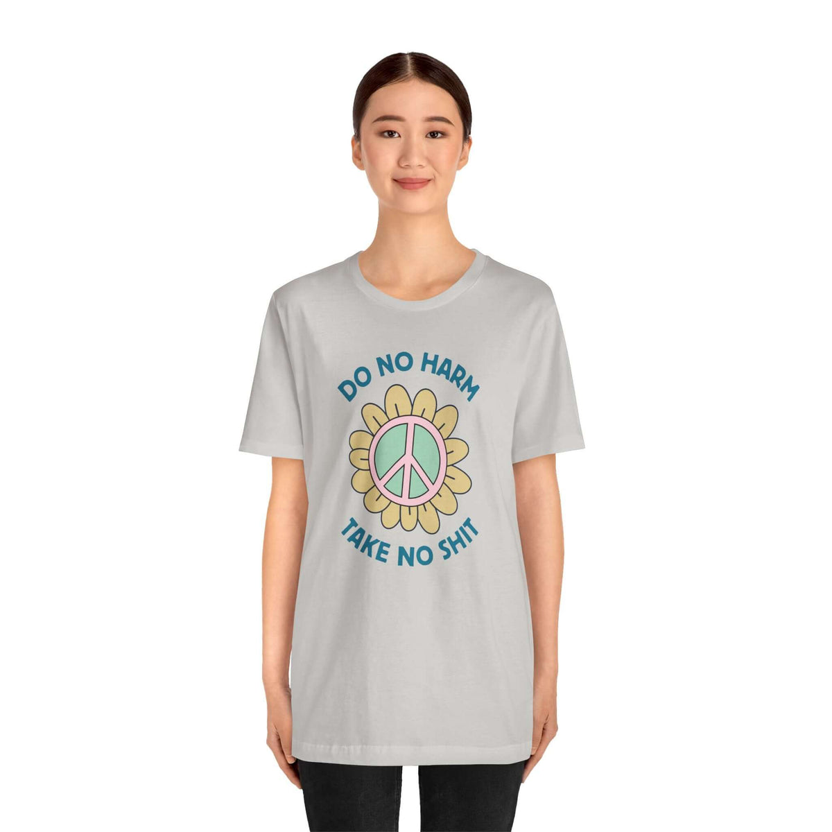 Model wearing a light gray Do No Harm Take No Shit Tee with a colorful peace flower design.