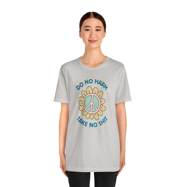 Model wearing a light gray Do No Harm Take No Shit Tee with a colorful peace flower design.