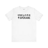Home Is in Spokane Tee featuring campfire, Bigfoot, and tree illustrations on a white t-shirt.