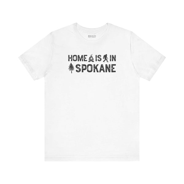 Home Is in Spokane Tee featuring campfire, Bigfoot, and tree illustrations on a white t-shirt.