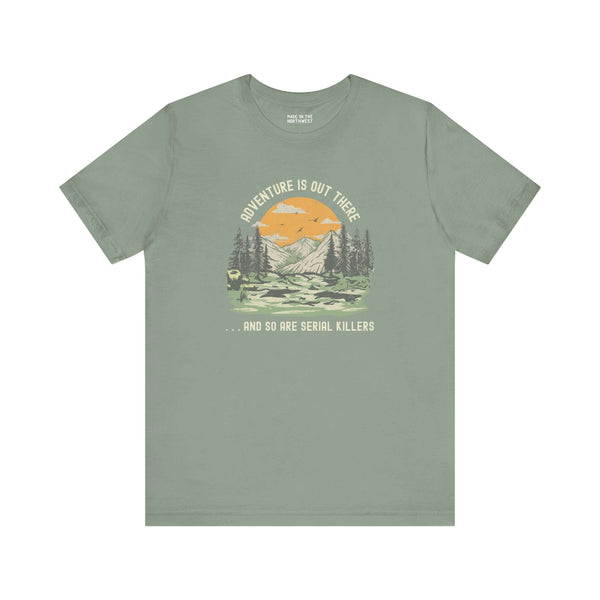 Premium soft tee featuring 'Adventure Is Out There... And So Are Serial Killers' graphic against a mountain backdrop.