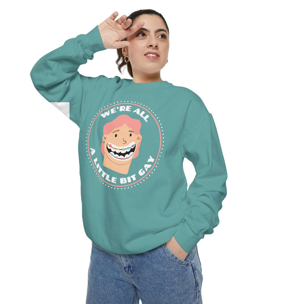 Woman wearing a teal sweatshirt that says "WE'RE ALL A LITTLE BIT GAY" featuring a playful graphic design.