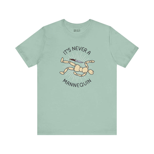 Mint green tee featuring graphic text 'It's Never a Mannequin' and cartoon mannequin, perfect for true crime fans.