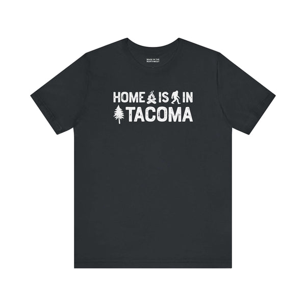 Home is in Tacoma tee featuring campfire, tree, and Bigfoot symbols on a black t-shirt.