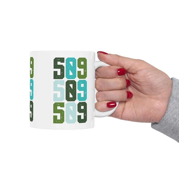 Hand holding a colorful Five-Oh-Nine Pop Spokane ceramic mug featuring the number 509 design.