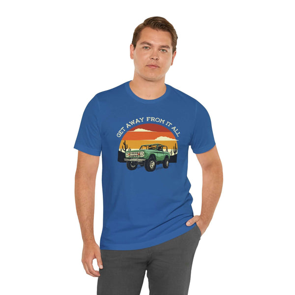 Man wearing a blue Get Away From It All tee featuring a vintage Bronco and sunset design.