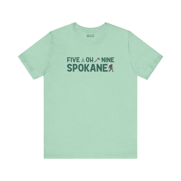 Mint green Spokane tee with "Five Oh Nine" text, small axe, and tree flourish. Celebrate Spokane pride with local charm.