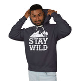 Stay Wild hoodie model wearing a dark sweatshirt with mountain and tree graphic for outdoor enthusiasts.