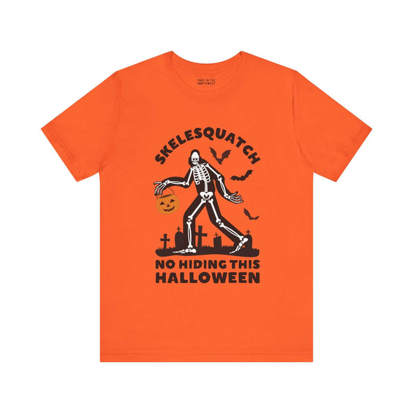 Orange Halloween tee featuring Skelesquatch skeleton Sasquatch with trick-or-treat bucket, bats, and graveyard design.