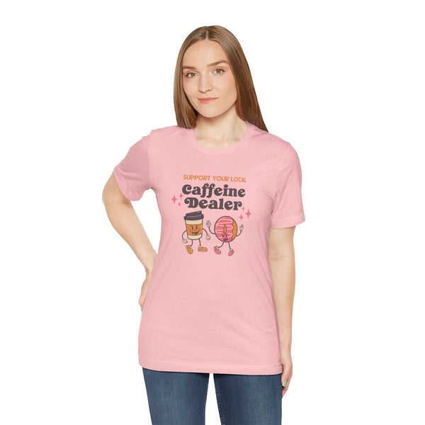 Woman wearing pink tee with 'Support Your Local Caffeine Dealer' design, celebrating local coffee culture.