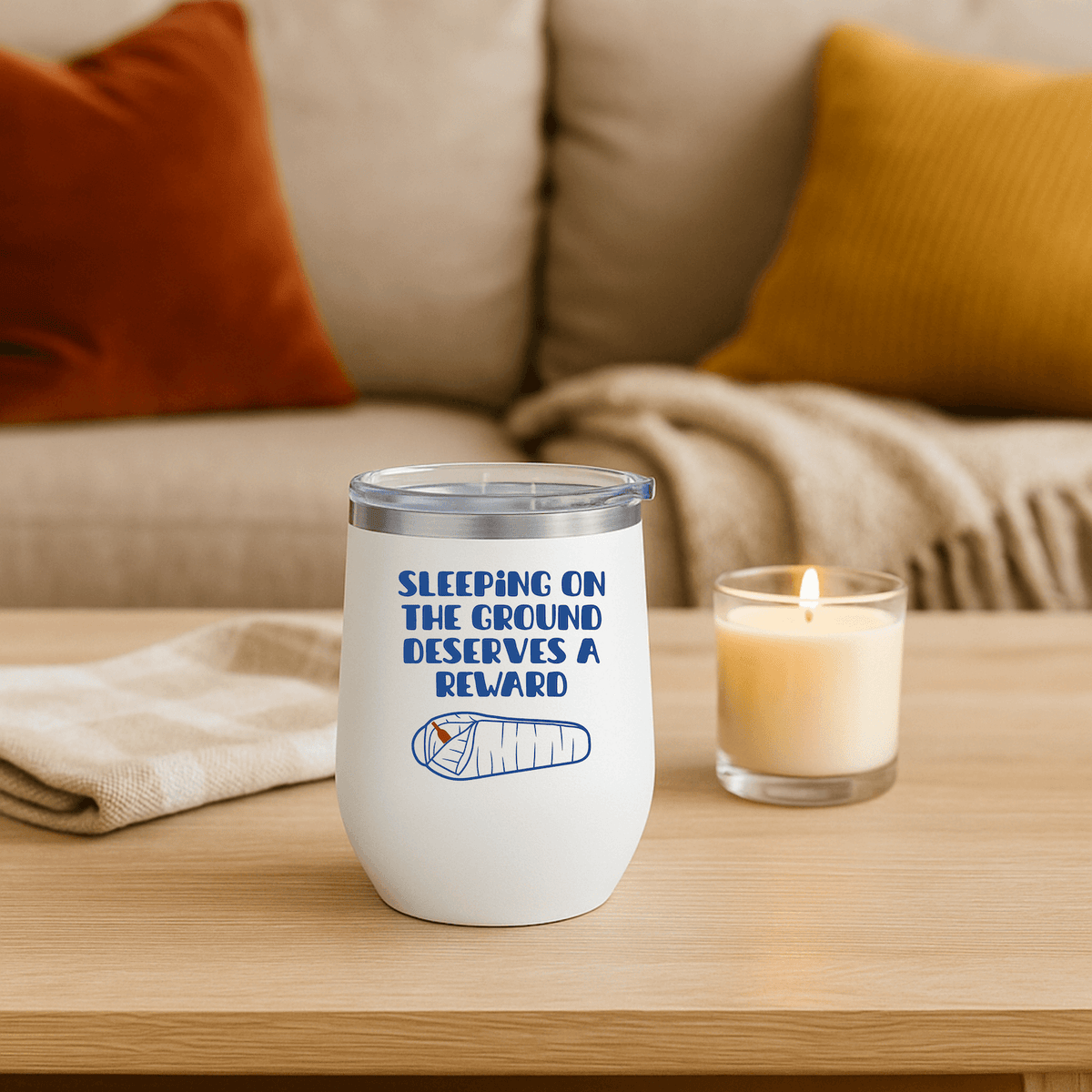 Sleeping on the Ground Deserves a Reward Camping Wine Tumbler 12 oz on a table beside a candle.