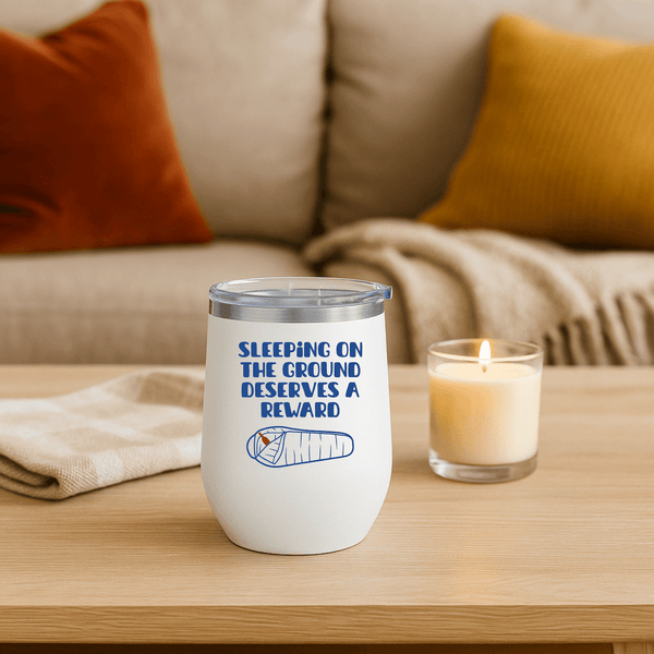 Sleeping on the Ground Deserves a Reward Camping Wine Tumbler 12 oz on a table beside a candle.